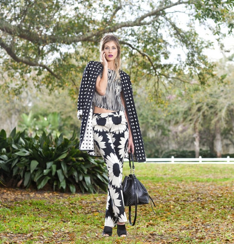 Adrianna from Modern Muse wears black and white sunflower print pants ($298) and a brush stroke print crop top ($188), both by Alice and Olivia. She also wears a pair of black satin mules ($328) by Kate Spade and a geometric black and white print coat ($1,590) by Akris Punto. Her black crystal-drop earrings ($425) are by Oscar de la Renta, while her black studded bucket bag ($3,350) is by Yves Saint Laurent. All are from Neiman Marcus Mall at Millenia.
